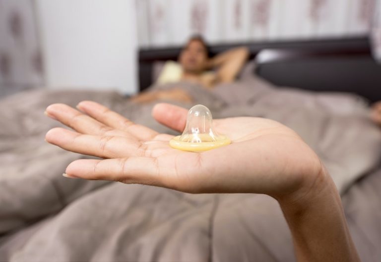 Eine Hand hält ein leeres Kondom ins Bild