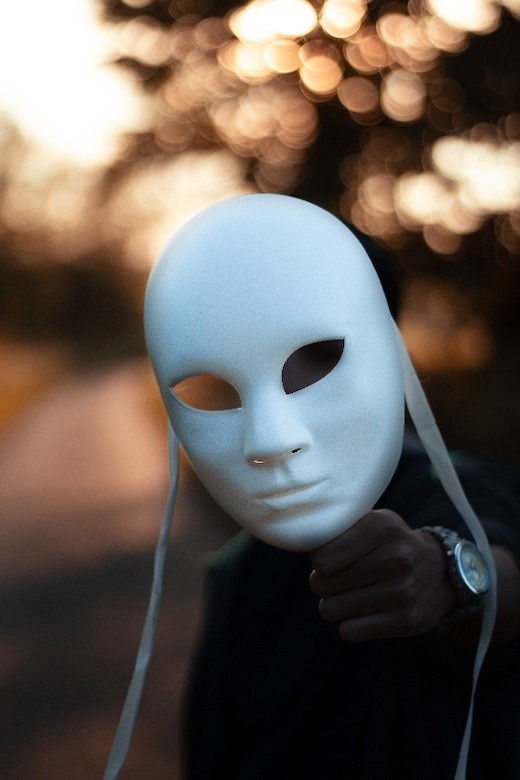 Eine Person hält eine Maske mit weißem Gesicht ins Bild